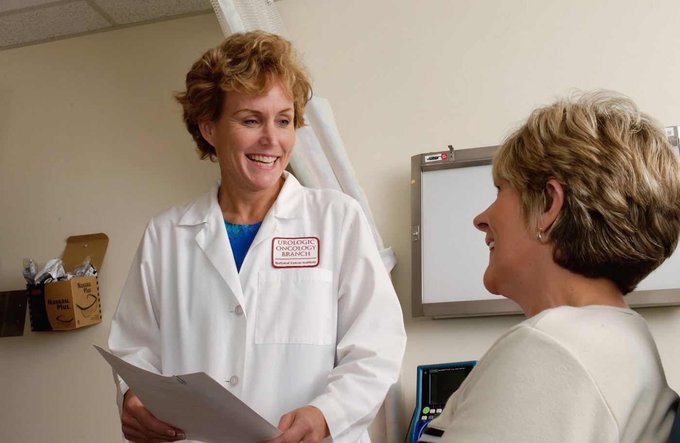 Physician in a white coat speaking with a patient in a clinic exam room